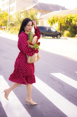 İyi alışverişler. Kırmızı elbiseli güzel beyaz bir kadının portresi. Elinde poşet dolusu alışveriş poşeti var..