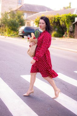 İyi alışverişler. Kırmızı elbiseli güzel beyaz bir kadının portresi. Elinde poşet dolusu alışveriş poşeti var..