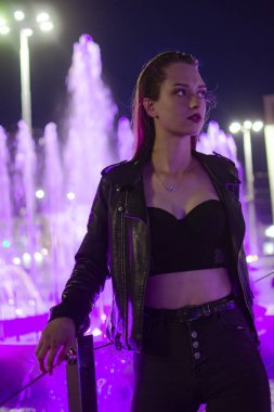 Brunette girl on the background of fountains. The girl stands at the fountains. Evening walk around the city.
