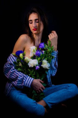 Brunette with flowers in her hands. young girl on a black background with flowers.