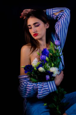 Brunette with flowers in her hands. young girl on a black background with flowers.
