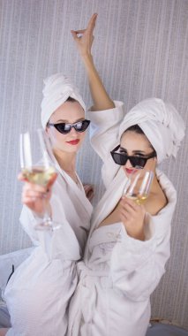 Bornozlu kızlar, kafalarında havlular ve güneş gözlükleriyle şarap içerler..