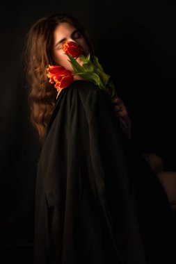 Güzel kırmızı laleler ellerinde siyah bir arka planda çiçek. Kadınlar ve Sevgililer Günü için tebrikler. Uluslararası Kadınlar Günü. Sevgililer Günü