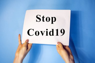 Mavi arkaplanda izole edilmiş beyaz bir kağıt var. Elinde Covid 19 yazan bir tabela var.