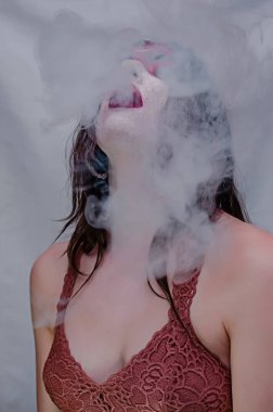 Siyah başlıklı yakışıklı bir adam sigara içiyor ve renkli pembe ve yeşil siyah bir izole arka plan üzerinde duman büyük bulutlar exhales