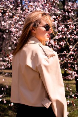 Baharda yürüyen uzun saçlı bir kadın. Kadın modası. Harika sakura açan ağaçtan hoşlanan bir kadın. Bahar yaşam tarzı, tatil ve seyahat.