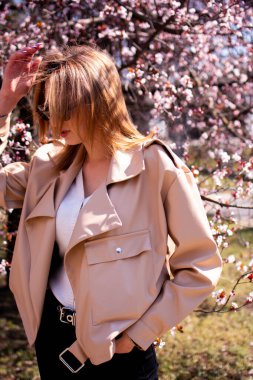 Baharda yürüyen uzun saçlı bir kadın. Kadın modası. Harika sakura açan ağaçtan hoşlanan bir kadın. Bahar yaşam tarzı, tatil ve seyahat.