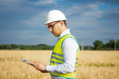 Tarım mühendisi tarlada, çiftçi elinde bir klasörle buğday tarlasında duruyor ve hasadı kontrol ediyor, mühendis tarlada buğdaylı bir tarlada duruyor, tarlada bir tarımcı.