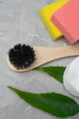 Brush for dry massage of the body, yellow and pink penza for the feet, cotton pads for the face, a green branch on a gray concrete background