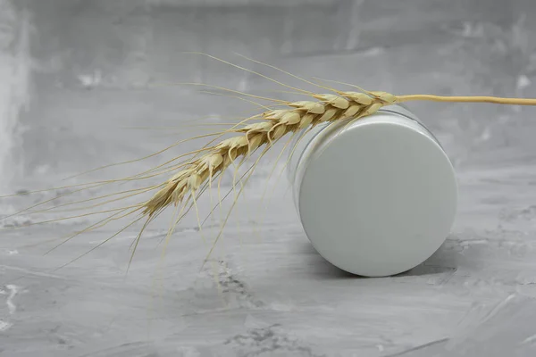 White jar of face cream, ear of wheat on a gray background, skin care cosmetics, skin care concept