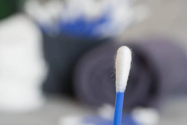 Close-up of a cotton swab, a macro photo of a cotton swab, blue cotton swabs, cotton pads for skin cleansing, a gray towel, a green branch of a plant on a gray background