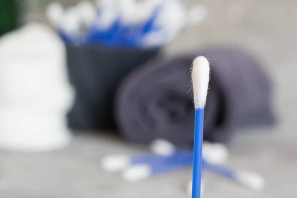 Close-up of a cotton swab, a macro photo of a cotton swab, blue cotton swabs, cotton pads for skin cleansing, a gray towel, a green branch of a plant on a gray background