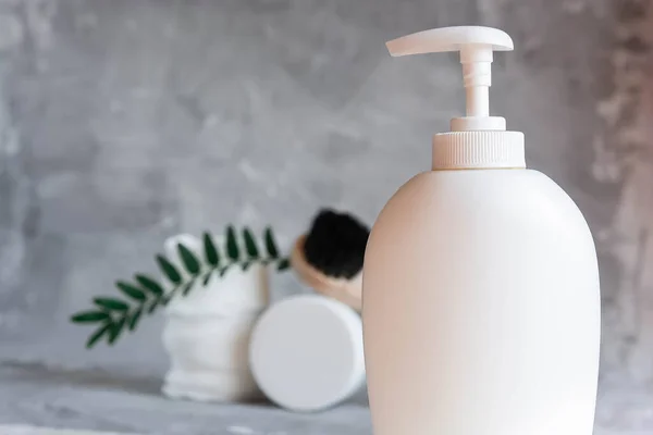 Care cosmetics on a gray background, a white jar of hair balm, a white jar of face cream, a black tube of lip balm, white cotton pads for removing makeup on a light gray background