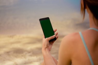 Spor üniformalı bir kız elinde bir telefon tutuyor, yeşil eşofman ve bisiklet şortu giyiyor, su dengesi, sokakta spor aktiviteleri, spor yaşam tarzı, parkta yoga, su kenarında esneme hareketleri yapıyor.