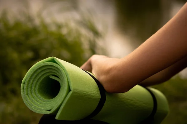 A girl in a sports uniform holds a yoga mat in her hands, dressed in a black sports top, a sports mat in green, yoga in the park, sports lifestyle, outdoor sports