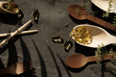 Masada ahşap kaplar, kaşıklar, çatallar, yiyecek için kepçeler, omega 3 vitaminler tahta kaşıkta yatıyor, spor, vitaminler, sağlıklı yaşam tarzı, beslenme malzemeleri, vitamin terapisi, spor malzemeleri