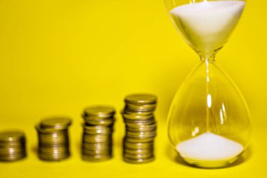 Kum saati ve bozuk para yığınının içinde akan kum. İş bitiş tarihi kavramı için geri sayım zamanlayıcısı.