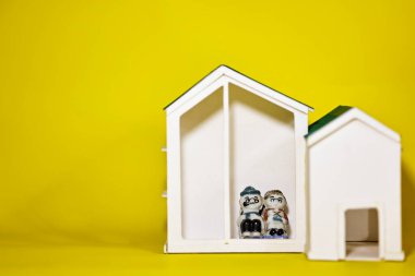 Minyatür bebek, ev ve kalp modelleri sarı arka planda. Gelecekteki kavramlar için emeklilik ve sağlık hizmetleri.