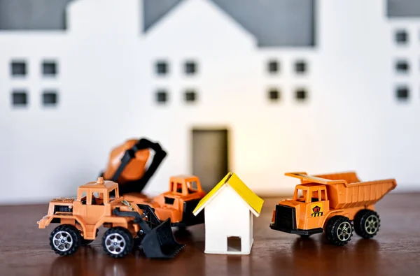 Miniature house models and construction truck models with glod coin on wooden table. Real estate developement or property investment. Construction industry business concept.