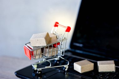İnternetten alışveriş ve teslimat konseptleri. Alışveriş arabasında paket kutuları ve ahşap masada dizüstü bilgisayarlar..