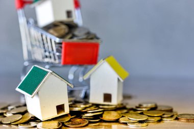 Minyatür ev ve alışveriş arabası. Masaya bozuk para dökülmüş. Gayrimenkul geliştirme veya gayrimenkul yatırımı. İnşaat endüstrisi iş konsepti.