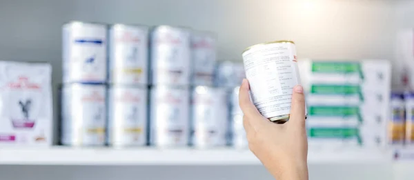 Women hand holding recovery canned food with defocus shelf background. Pet care concept
