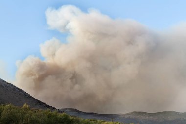 Gri duman bulutu dağların üzerinde açık havada güneşli bir günde mavi gökyüzünü kaplar. Sıcak gün konseptinde yangın tehlikesi