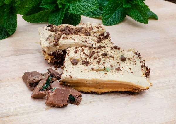 Traditional South African layered peppermint crisp tart or dessert on light wooden surface with fresh mint in background and peppermint chocolate pieces