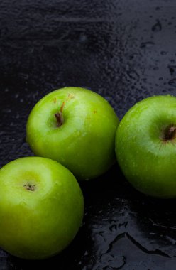 Taze ve çıtır çıtır yeşil büyükanne siyah yüzey üzerinde su damlacıkları olan demirci elmaları.
