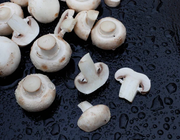 White button mushrooms on black surface with water droplets