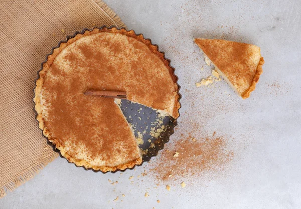Traditional South African milk tart freshly baked and in tin. Mottled grey and rustic surface with copy space