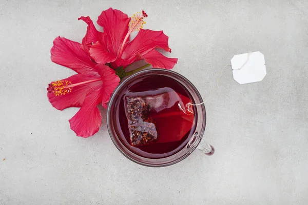 Bright and flavorful hibiscus tea in a glass cup, with hibiscus flower and copy space