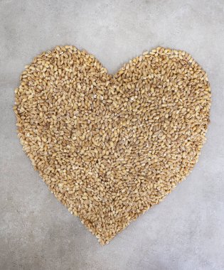 Benekli gri bir yüzey üzerindeki buğday tanelerinden yapılmış kalp