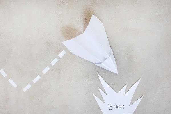 Paper airplane as metaphor, heading for a crash or explosion, on grey with copy space