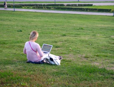Şehirdeki çimlerin üzerinde dizüstü bilgisayarda çalışan bir kız.