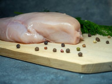 Siyah arka planda kesme tahtasındaki tavuk göğsü filetosu. Biberli mısır ve bir parça etin etrafında dereotu. Tavuk pişiriyorum.