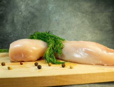 Kesme tahtasındaki tavuk göğsü filetosu. Siyah arka planda hala hayat var. Bir et parçasının etrafında çok renkli biberler. Tavuk pişiriyorum. Çiğ et