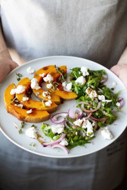 Adam bir tabak dolusu kabak, roka ve peynir tutuyor.