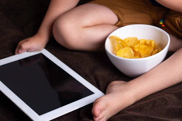 bir çocuk ve bir tablet, bir gadget'ı tutan yiyor patates cipsi, zararlı gıda ve gadget'üzerindeki bağımlılığı bir kavram