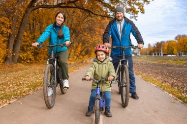 Sonbahar parkında çocuklu bir aile bisiklete biniyor.