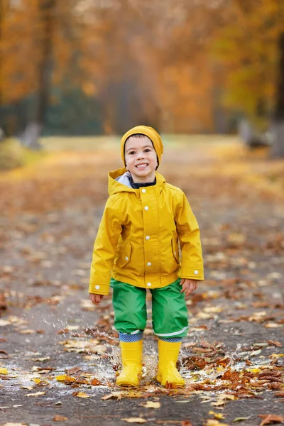 快乐的小男孩，黄色的雨衣在水坑里跳跃 — 图库照片