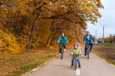 Sonbahar parkında çocuklu bir aile bisiklete biniyor.