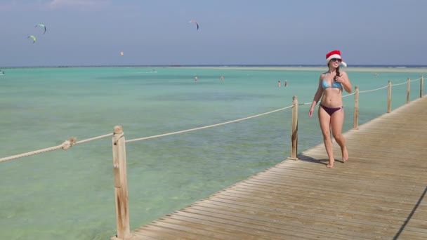 Smiling young woman in santa hat on walking on wooden pontoon — Stock Video