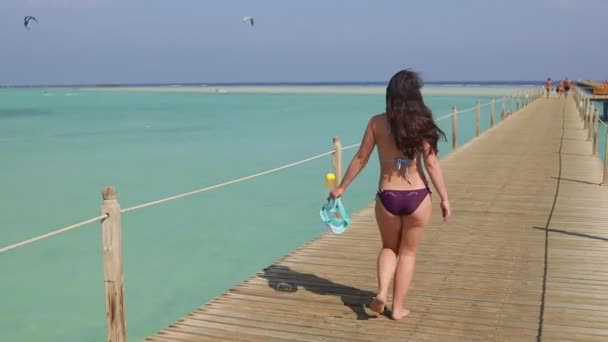 En lykkelig ung kvinne med snorkelmaske som går på en pongtong av tre i havet – stockvideo