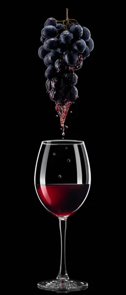 Красное вино, наливаемое в бокал из винограда — стоковое фото