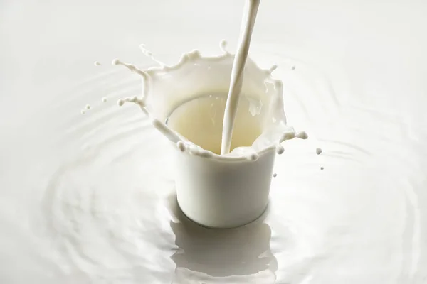 Milk pouring into glass with splashes on white background — Stock Photo, Image