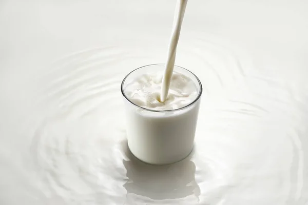 Leche vertiendo en el vidrio sobre fondo blanco — Foto de Stock