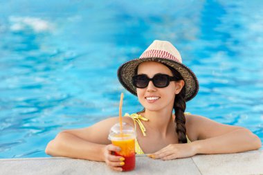 Gülümseyen kadın yüzme havuzunda meyve suyu içiyor.