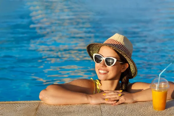 Gülümseyen kadın yüzme havuzunda meyve suyu içiyor.