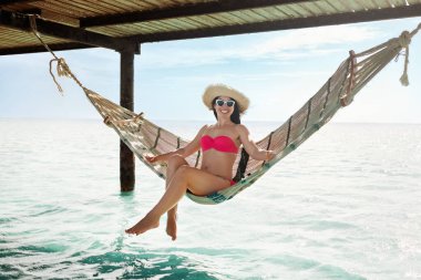 Hamakta sallanan mutlu genç bir kadın. Arka planda deniz var.